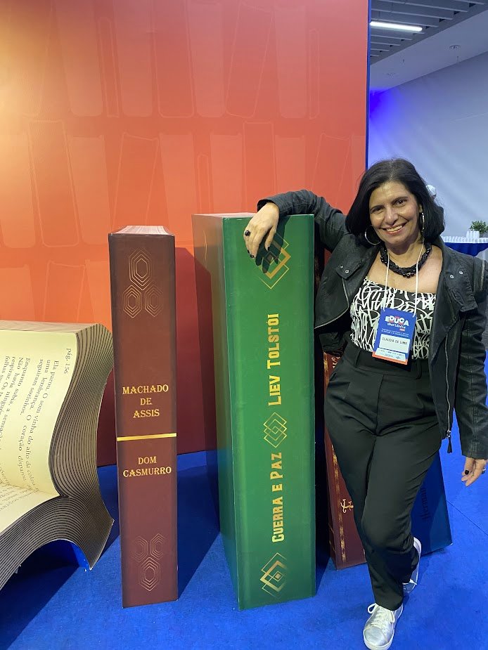 Claudia Turatti em pé, sorrindo, ao lado de esculturas de livros de dois metros de altura